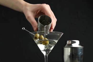 Photo of Woman making martini cocktail with olives on black background, closeup