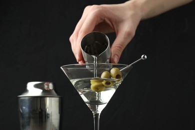 Photo of Woman making martini cocktail with olives on black background, closeup