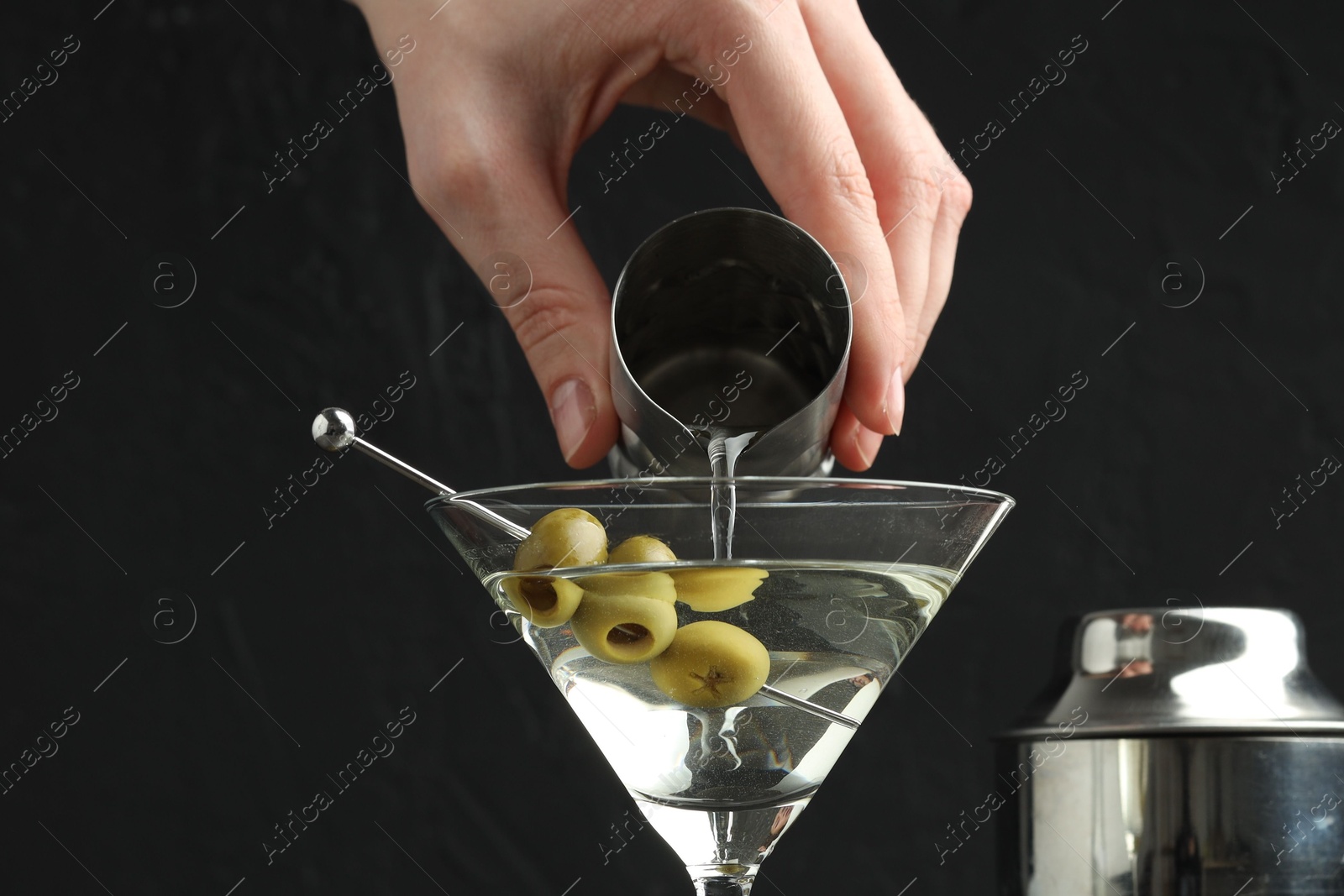 Photo of Woman making martini cocktail with olives on black background, closeup