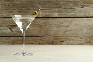 Photo of Martini cocktail with olives in glass on light table, space for text