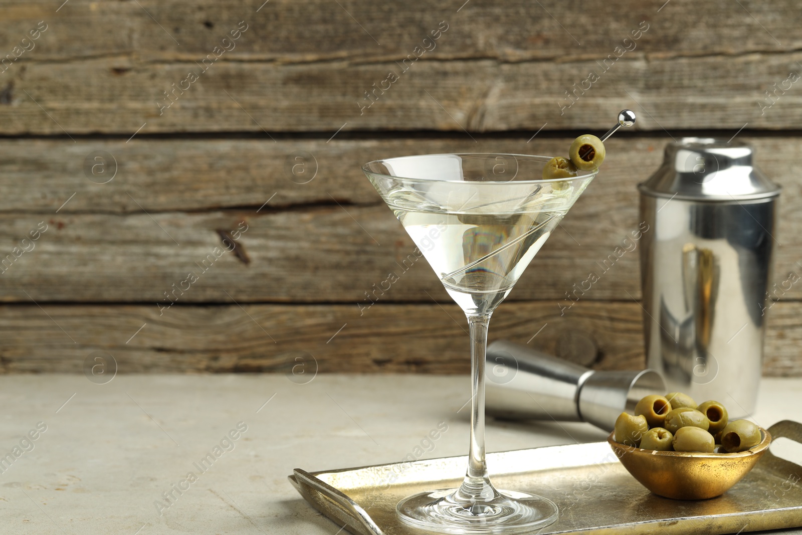 Photo of Martini cocktail with olives in glass and shaker on light table, space for text