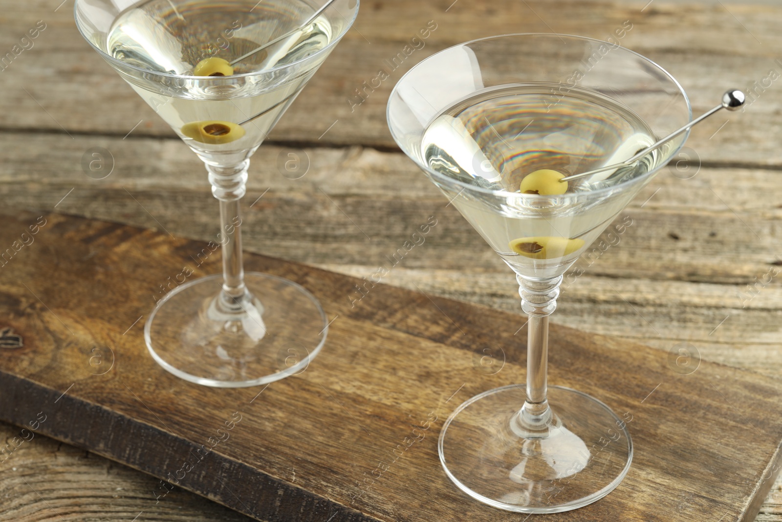 Photo of Martini cocktail with olives in glasses on wooden table, closeup