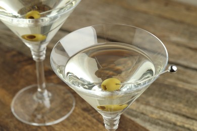 Photo of Martini cocktail with olives in glasses on wooden table, closeup