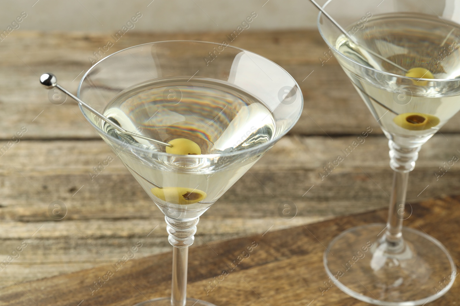 Photo of Martini cocktail with olives in glasses on wooden table, closeup