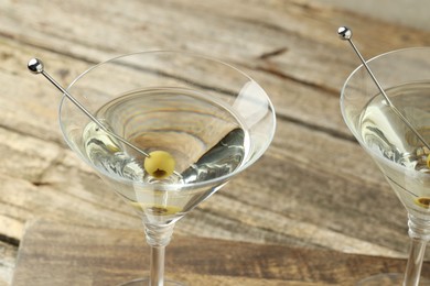 Photo of Martini cocktail with olives in glasses on wooden table, closeup