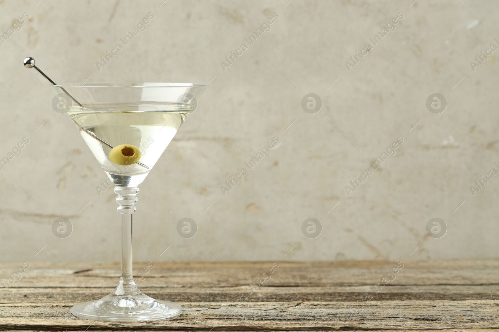 Photo of Martini cocktail with olive in glass on wooden table, space for text