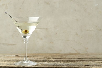 Photo of Martini cocktail with olive in glass on wooden table, space for text