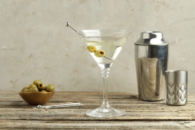 Photo of Martini cocktail with olives in glass and shaker on wooden table