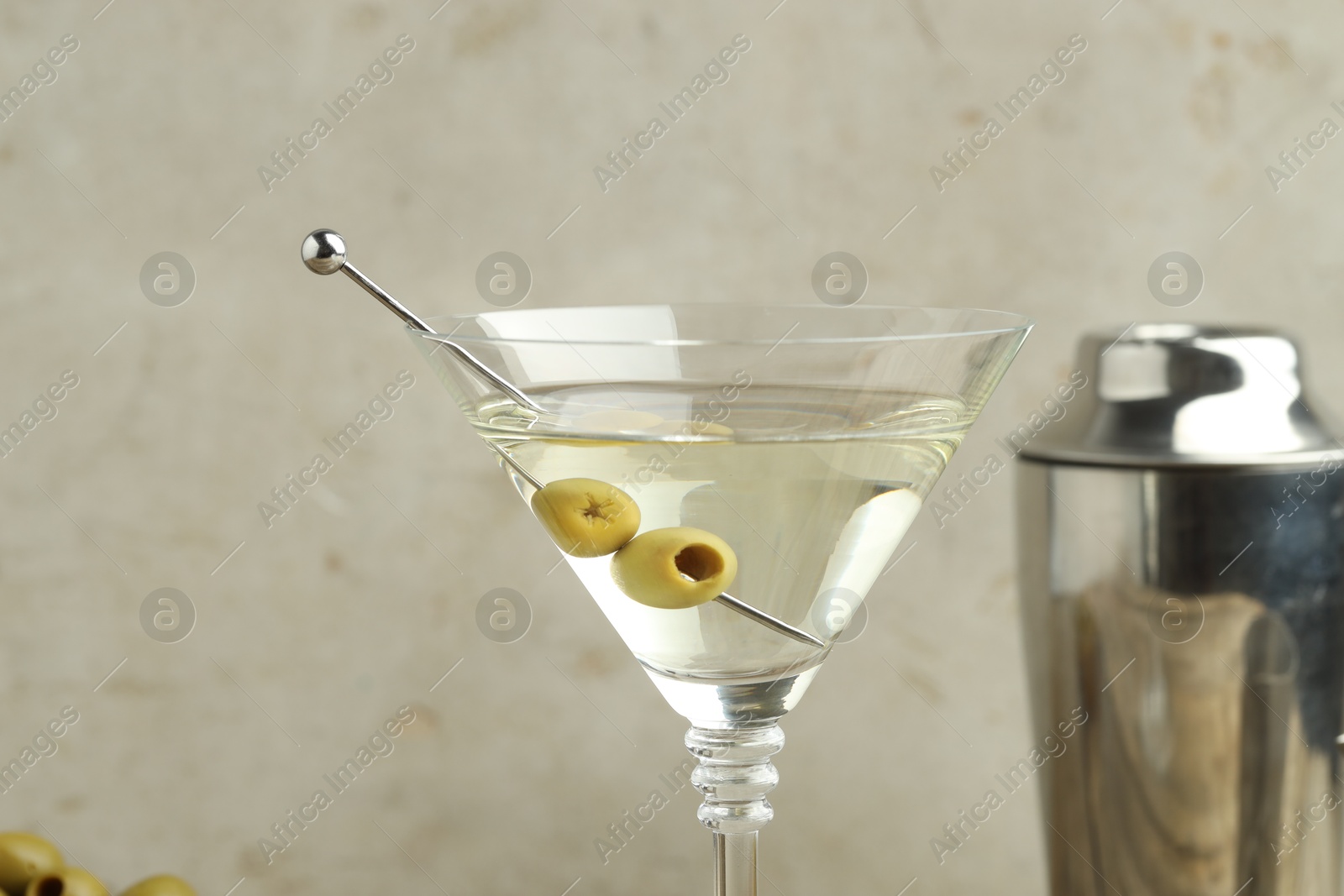 Photo of Martini cocktail with olives in glass and shaker on light background, closeup