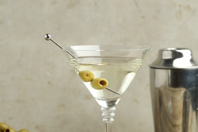 Photo of Martini cocktail with olives in glass and shaker on light background, closeup