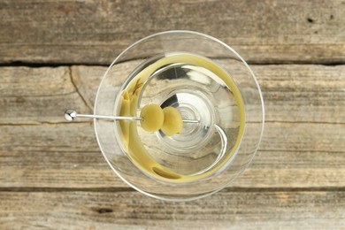 Photo of Martini cocktail with olives in glass on wooden table, top view