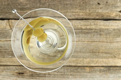 Photo of Martini cocktail with olives in glass on wooden table, top view. Space for text