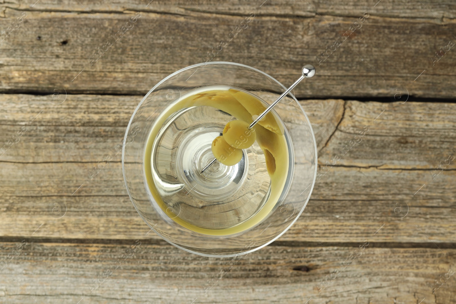 Photo of Martini cocktail with olives in glass on wooden table, top view