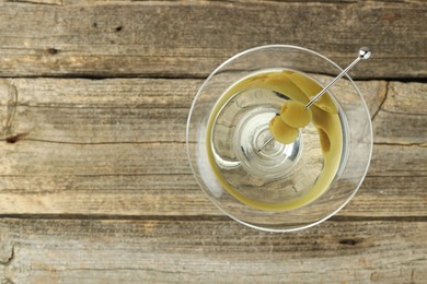 Photo of Martini cocktail with olives in glass on wooden table, top view. Space for text