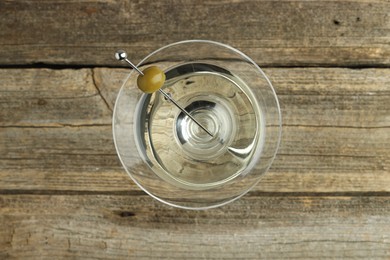 Photo of Martini cocktail with olive in glass on wooden table, top view