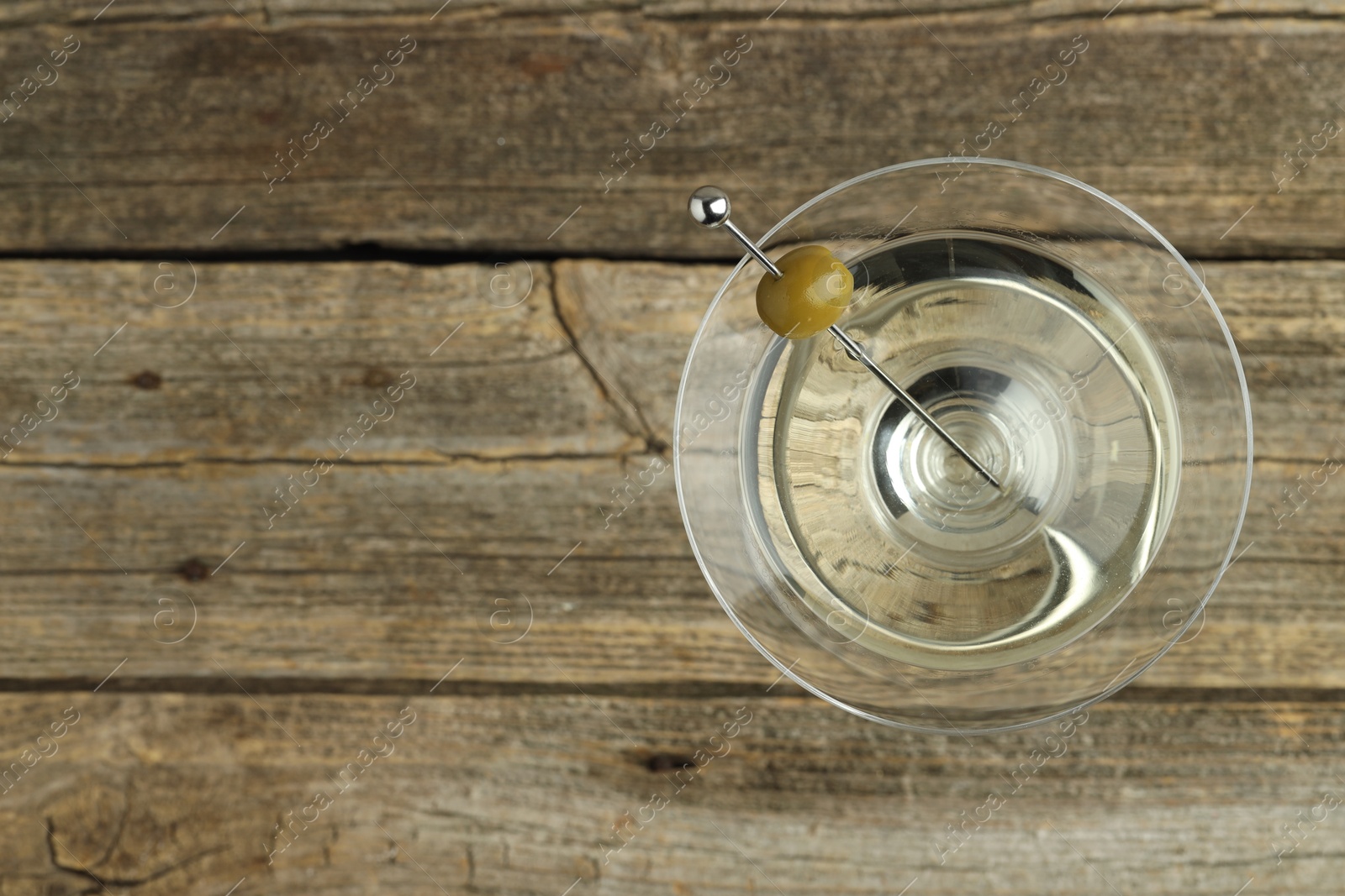 Photo of Martini cocktail with olive in glass on wooden table, top view. Space for text