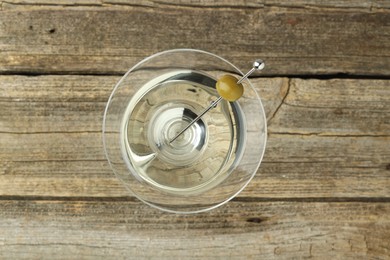 Photo of Martini cocktail with olive in glass on wooden table, top view