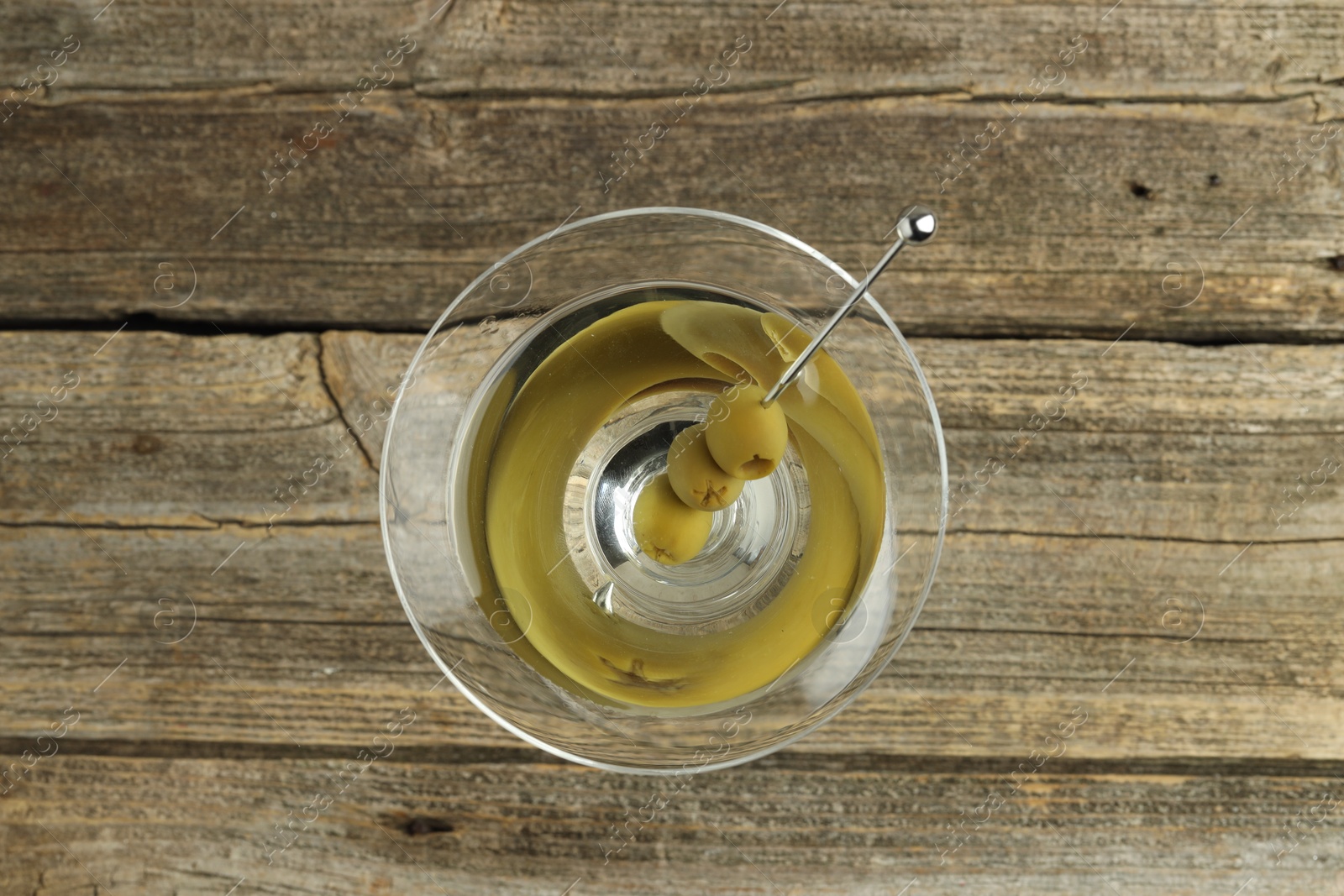 Photo of Martini cocktail with olives in glass on wooden table, top view