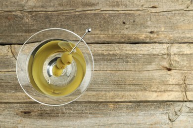 Photo of Martini cocktail with olives in glass on wooden table, top view. Space for text