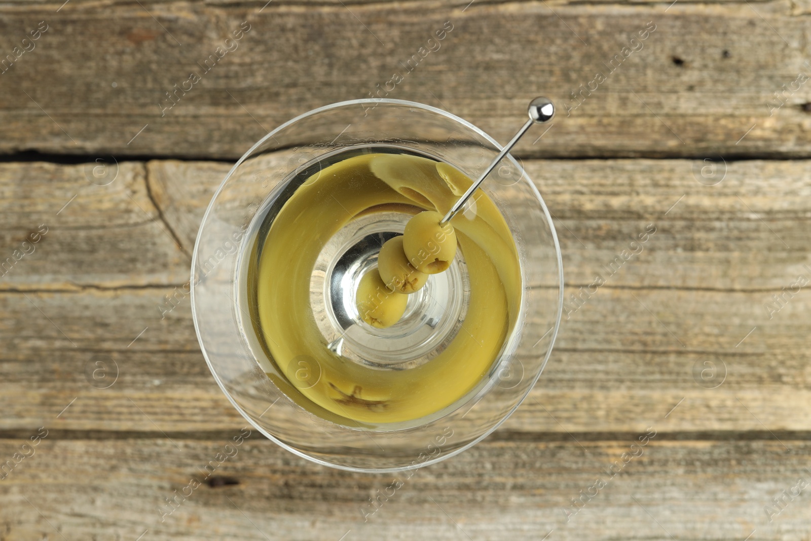 Photo of Martini cocktail with olives in glass on wooden table, top view