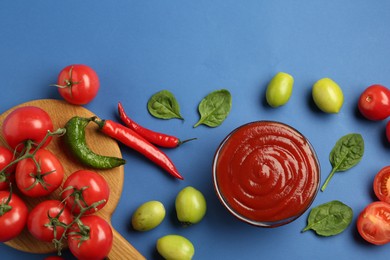 Photo of Tasty ketchup and vegetables on blue background, flat lay