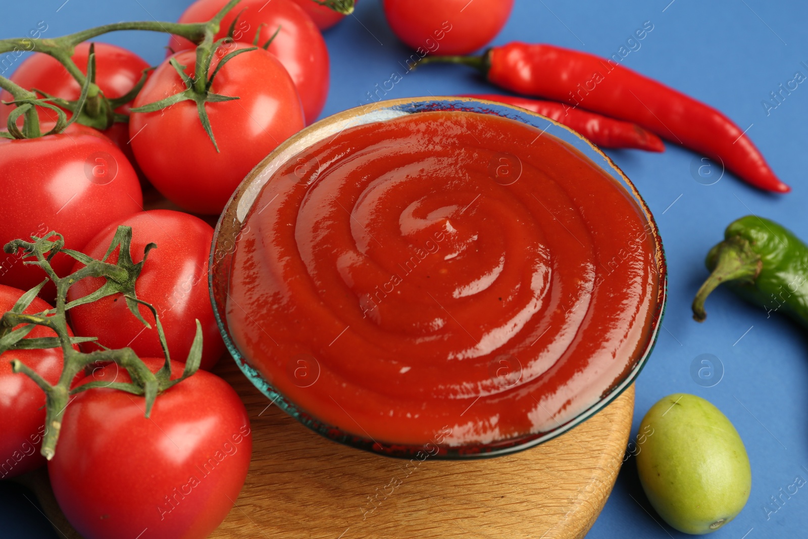 Photo of Tasty ketchup and vegetables on blue background, closeup