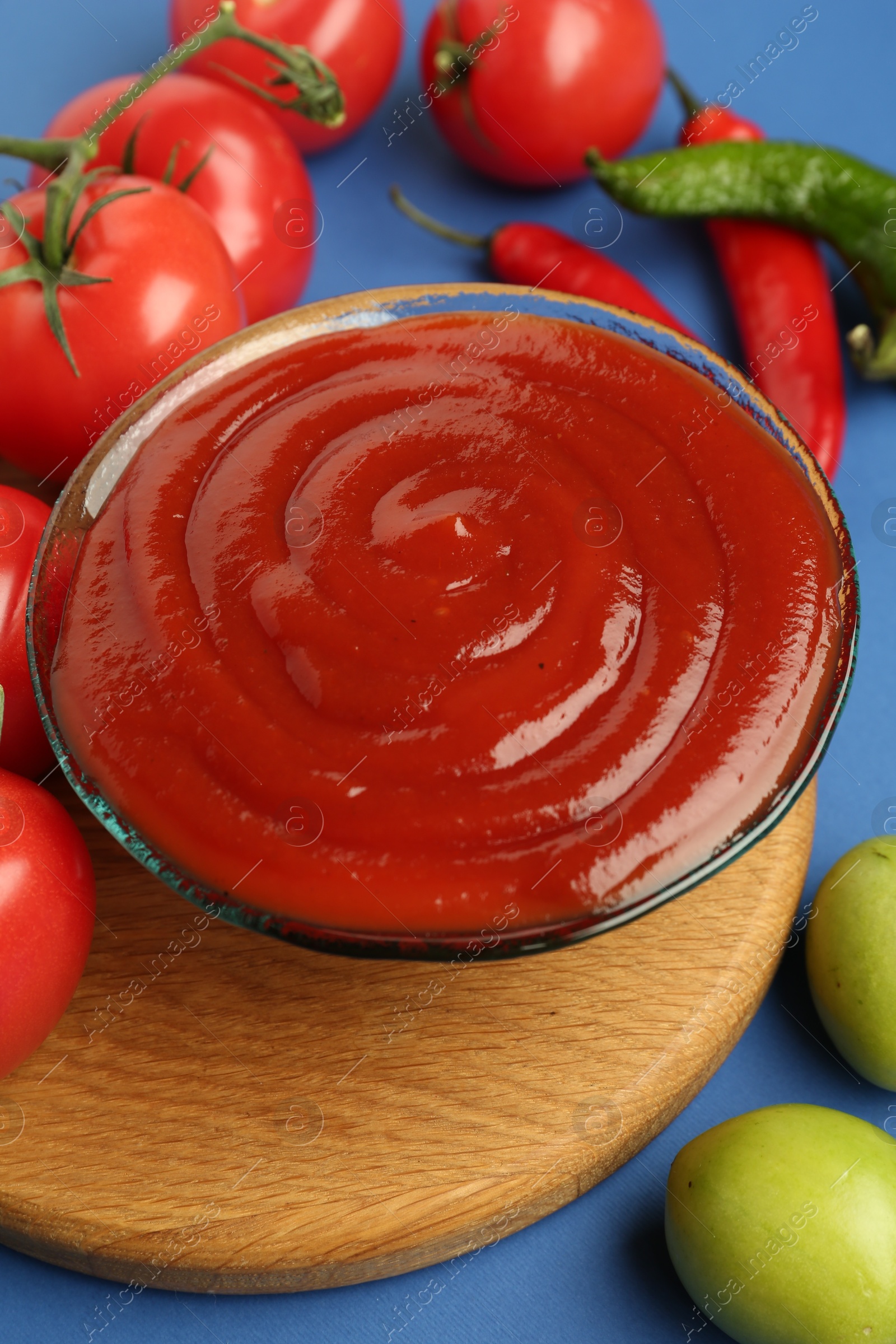 Photo of Tasty ketchup and vegetables on blue background, closeup