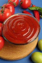 Photo of Tasty ketchup and vegetables on blue background, closeup