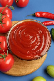 Photo of Tasty ketchup and vegetables on blue background, above view