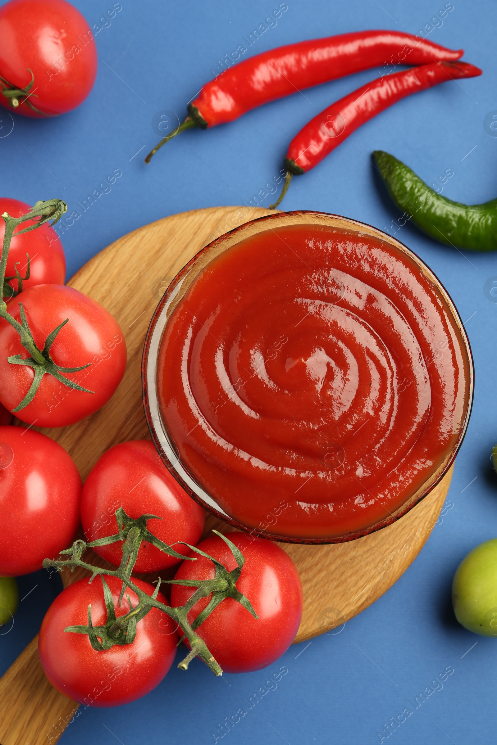 Photo of Tasty ketchup and vegetables on blue background, flat lay