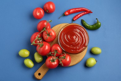 Photo of Tasty ketchup and vegetables on blue background, flat lay