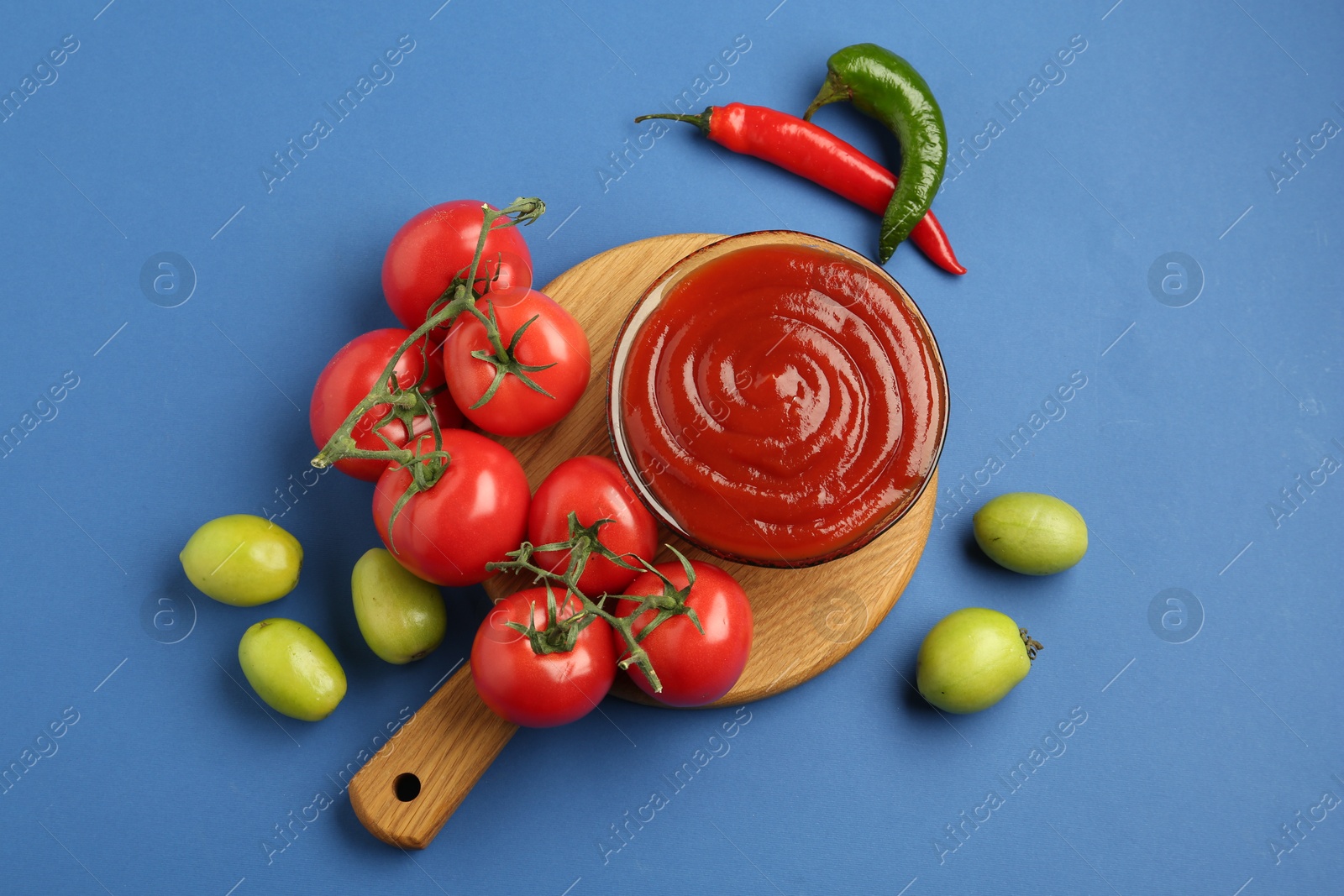 Photo of Tasty ketchup and vegetables on blue background, flat lay