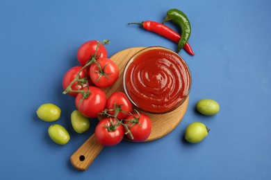 Photo of Tasty ketchup and vegetables on blue background, flat lay