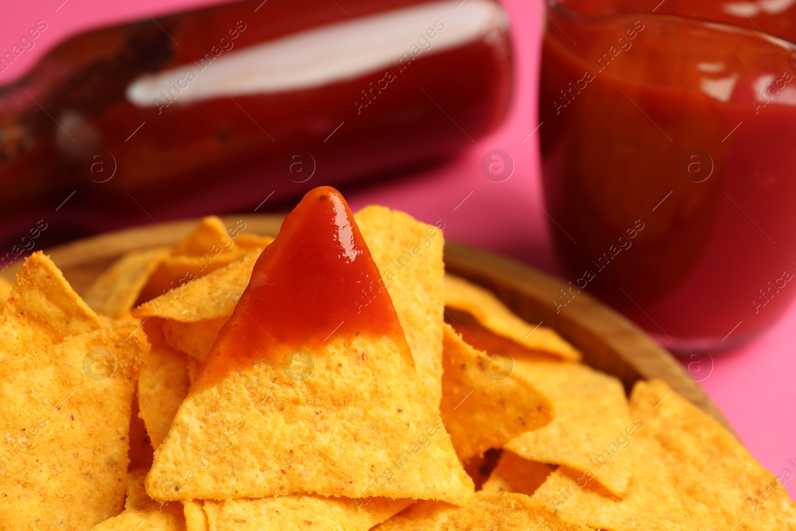 Photo of Tasty ketchup and nachos on pink background, closeup