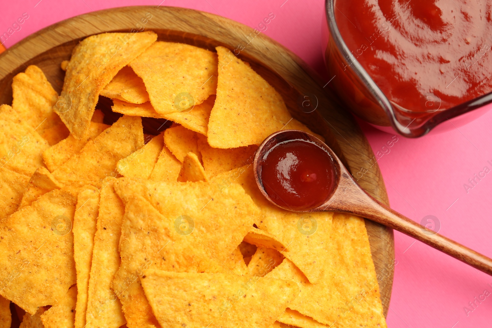 Photo of Tasty ketchup and nachos on pink background, top view