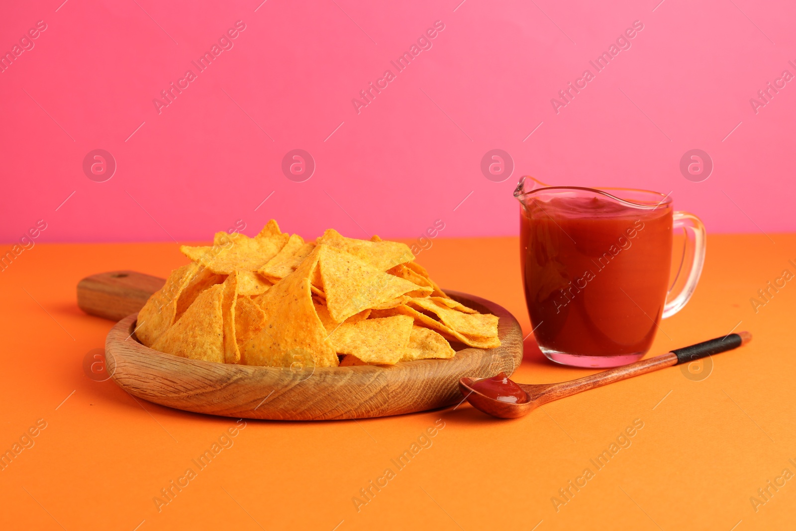 Photo of Tasty ketchup and nachos on pink background