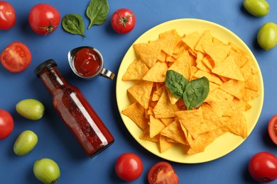 Photo of Tasty ketchup, nachos, tomatoes and basil on blue background, flat lay