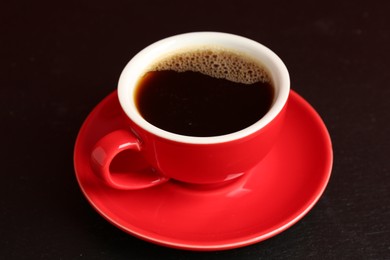 Photo of Red cup with coffee on black table, closeup