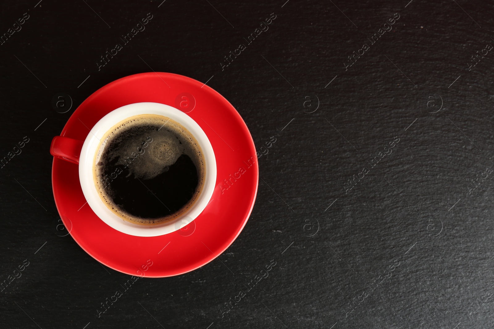 Photo of Red cup with coffee on black table, top view. Space for text