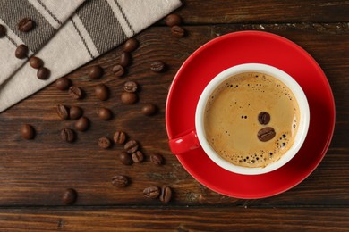 Photo of Red cup with coffee and roasted beans on wooden table, top view. Space for text