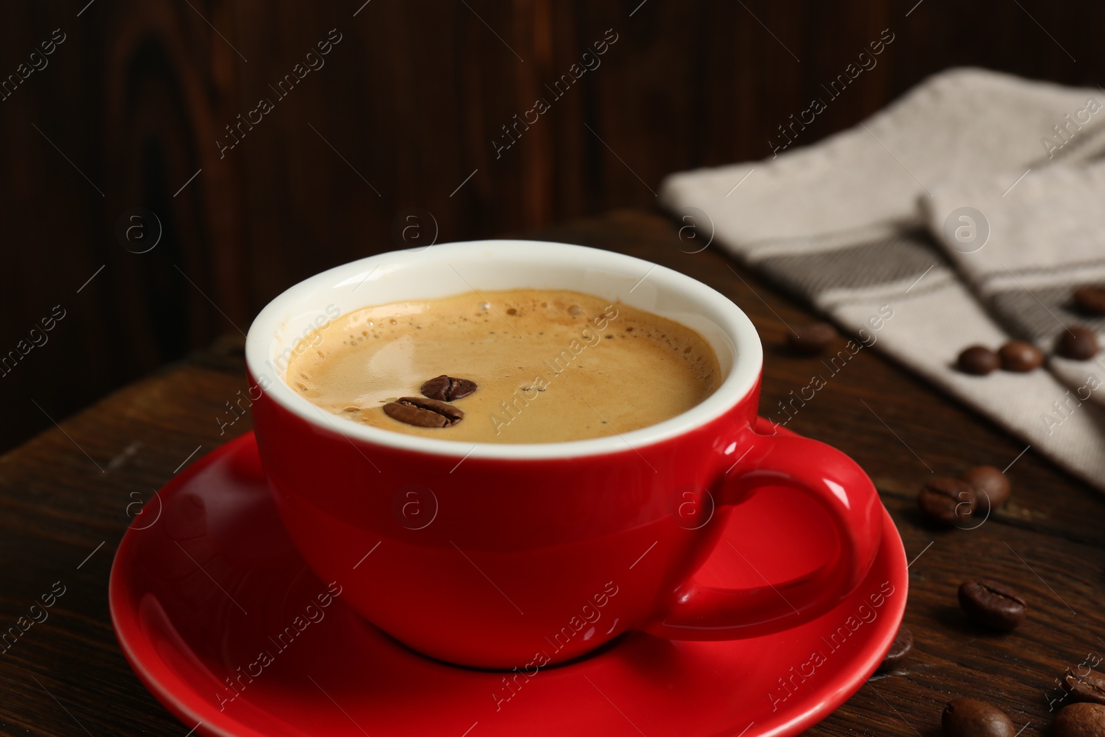 Photo of Red cup with coffee and roasted beans on wooden table, closeup