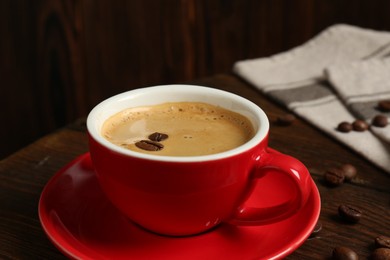 Photo of Red cup with coffee and roasted beans on wooden table, closeup