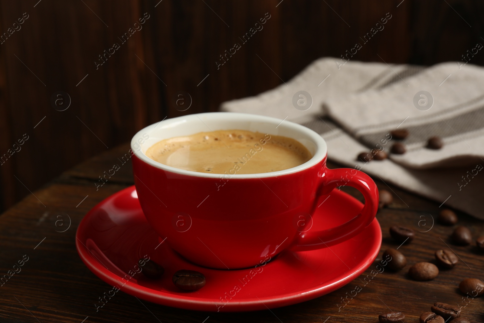 Photo of Red cup with coffee and roasted beans on wooden table, closeup