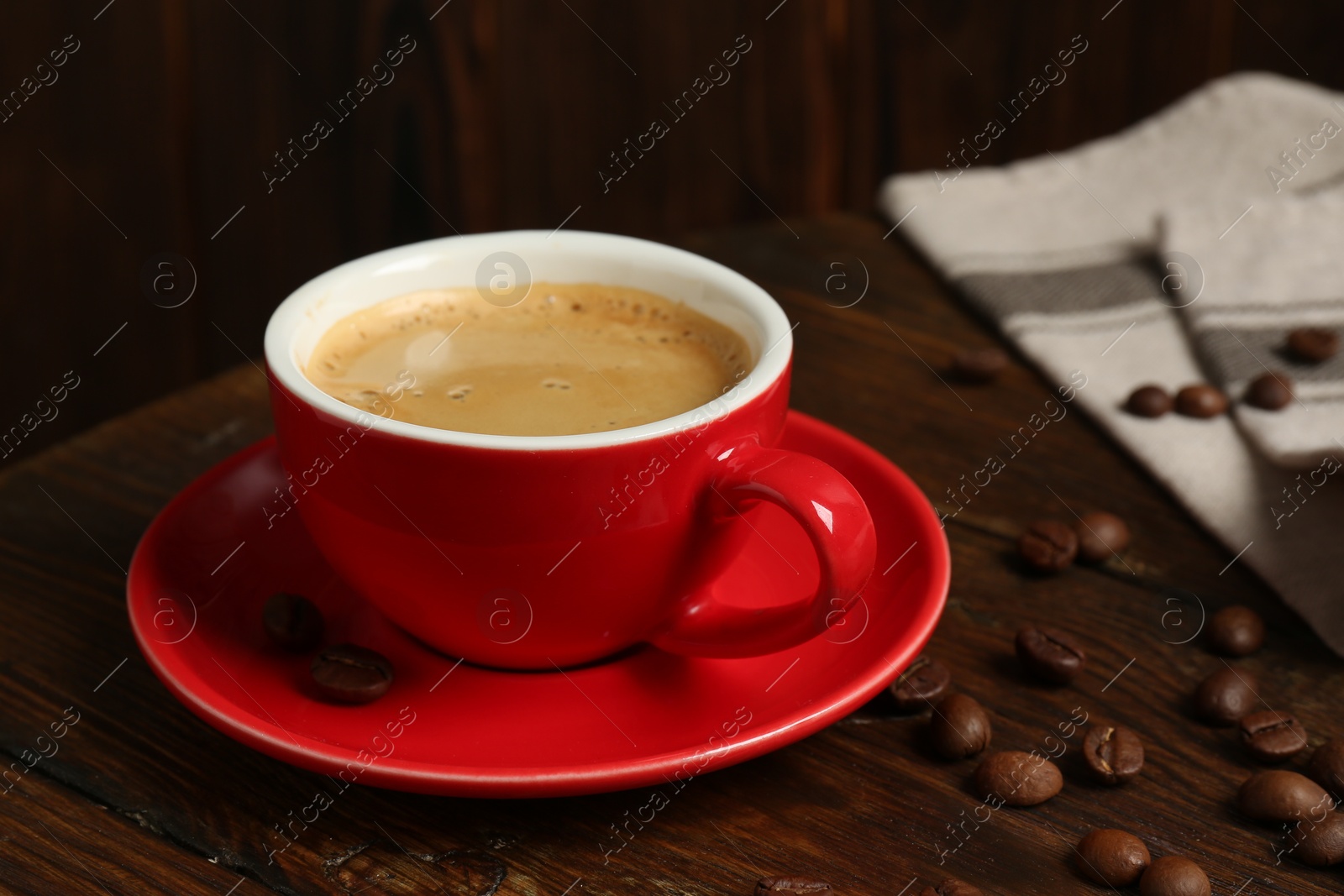 Photo of Red cup with coffee and roasted beans on wooden table, closeup