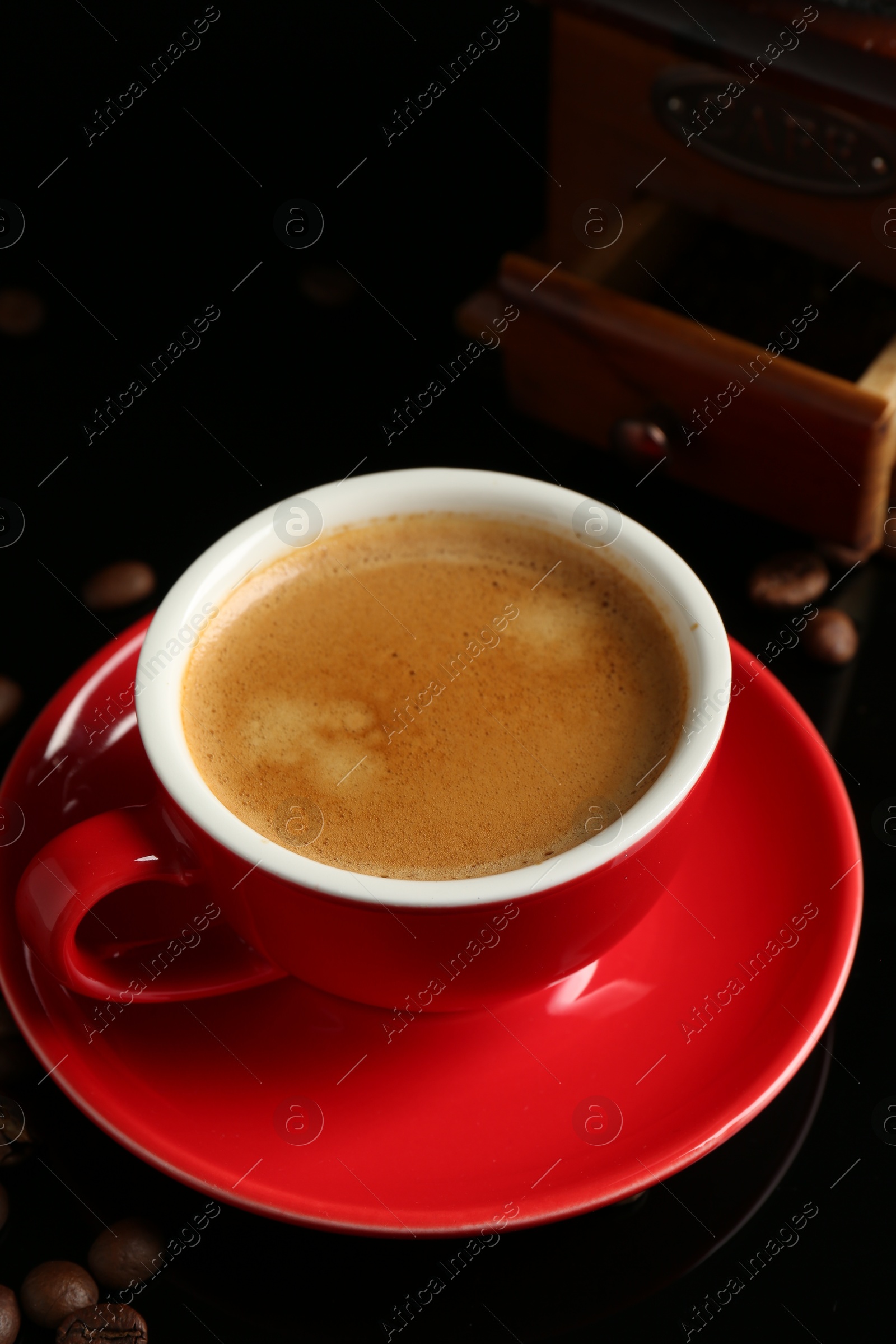 Photo of Red cup with coffee, roasted beans and vintage grinder on black background, closeup