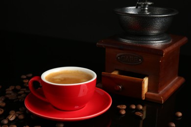 Photo of Red cup with coffee, roasted beans and vintage grinder on black background