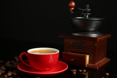 Photo of Red cup with coffee, roasted beans and vintage grinder on black background