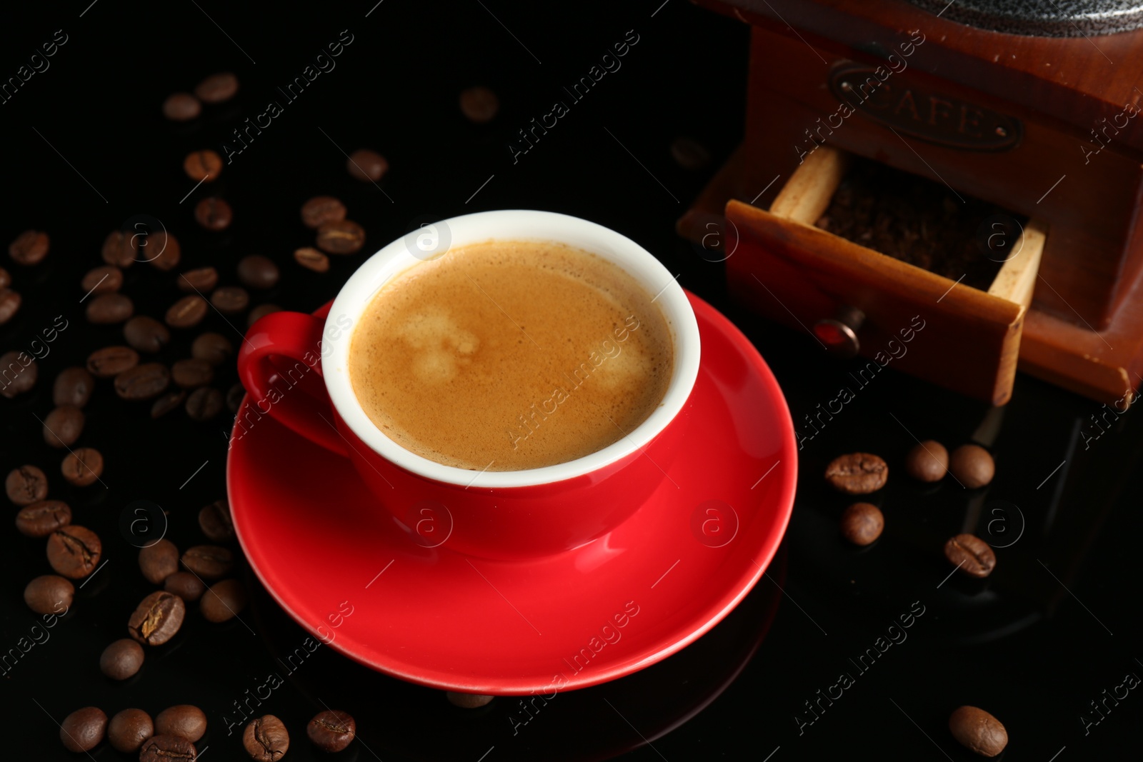 Photo of Red cup with coffee, roasted beans and vintage grinder on black background