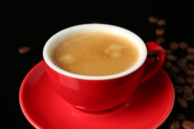 Photo of Red cup with coffee and roasted beans on black background, closeup