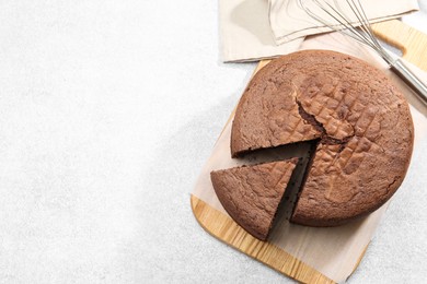 Photo of Cut chocolate sponge cake and whisk on light table, top view. Space for text